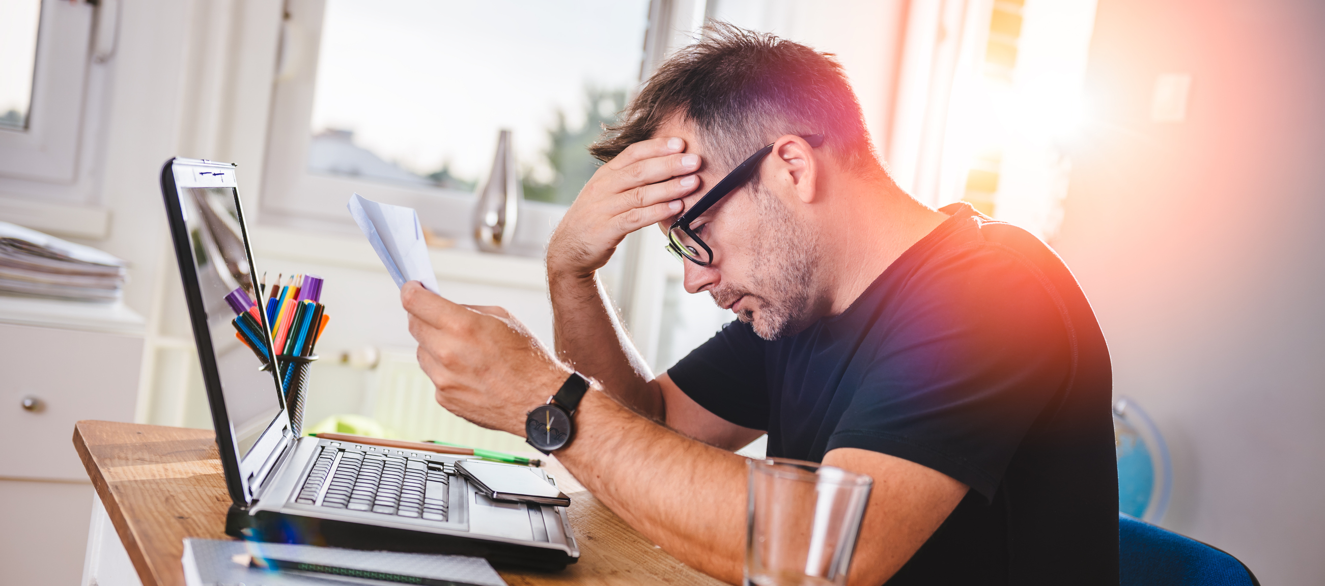 Man with laptop and documents holding head