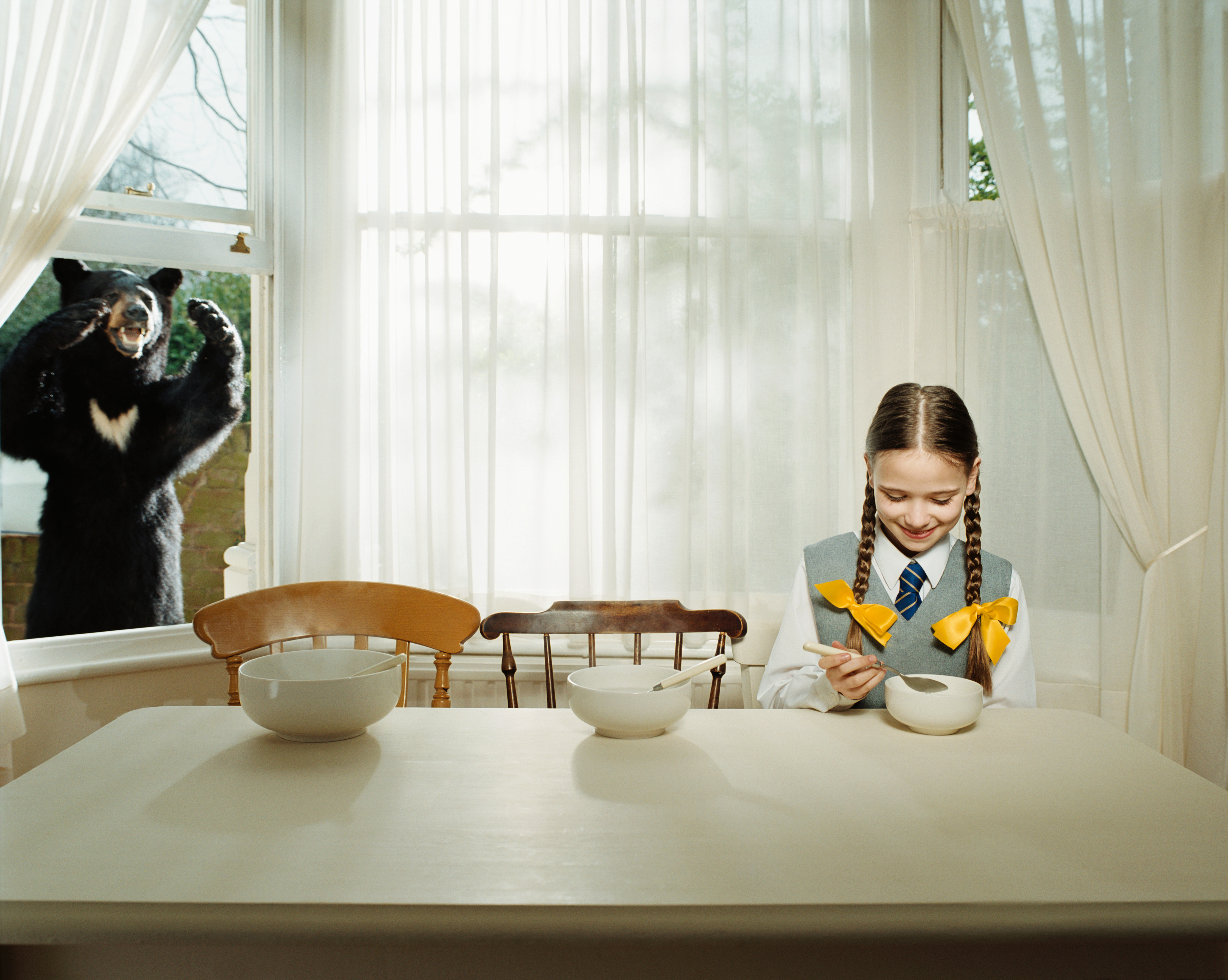 Goldilocks eating porridge while a bear watches.