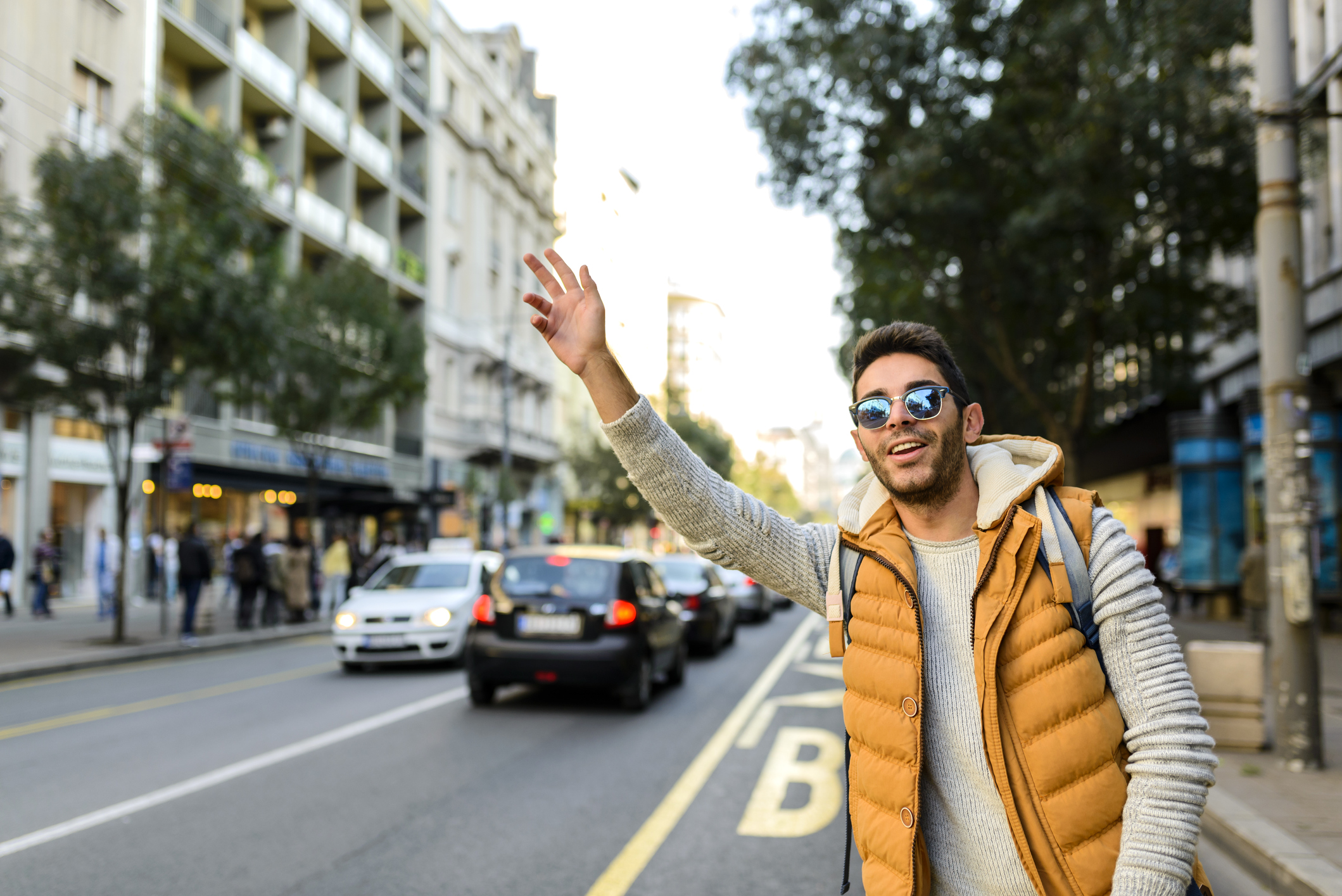 A young man reaches his hand up to hail a car