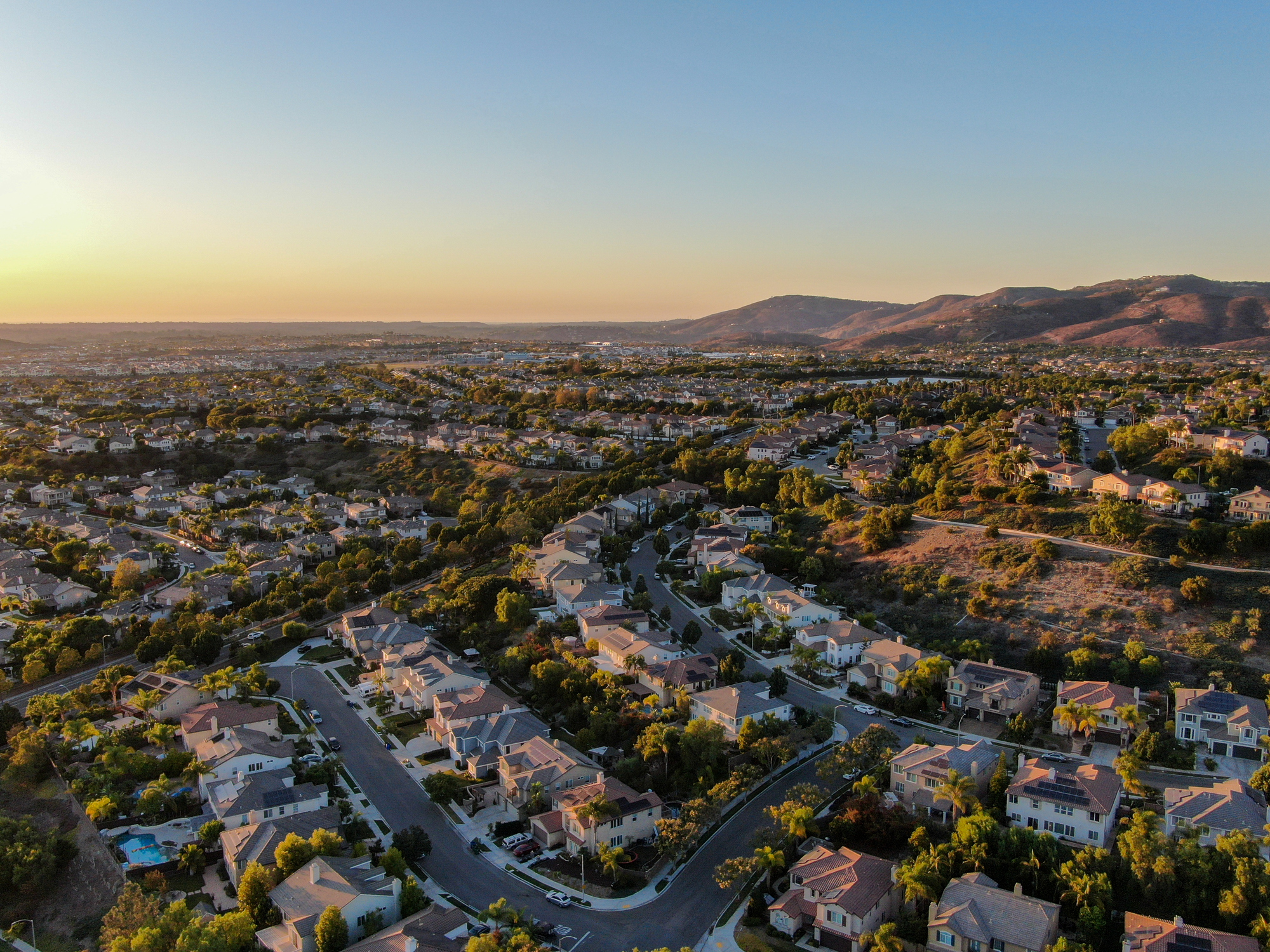 An overhead shot of a subdivision at sunset with a small a mountain in the distant background.