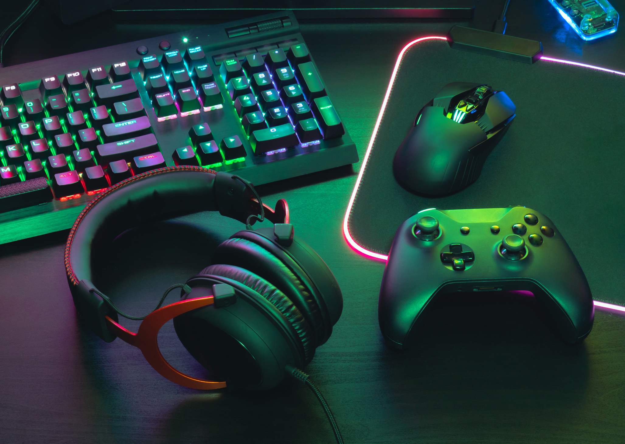 A gaming setup with console, mouse, keyboard, and earphones, glowing in multiple colors.