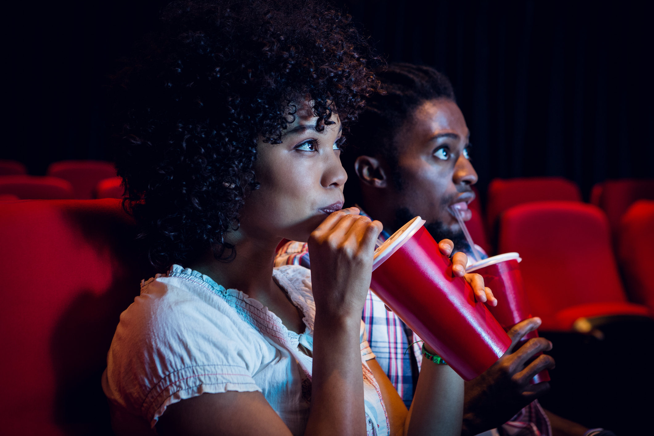 Two people drinking sodas in a movie theater.