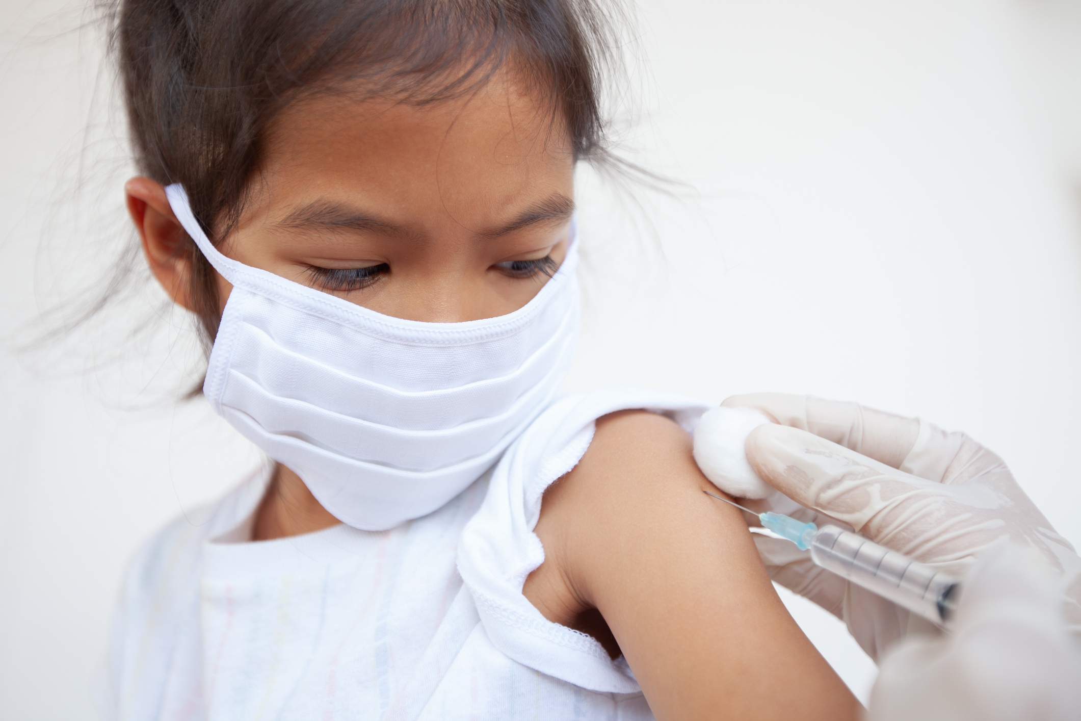 A girl wearing a mask receives an injection in her arm.