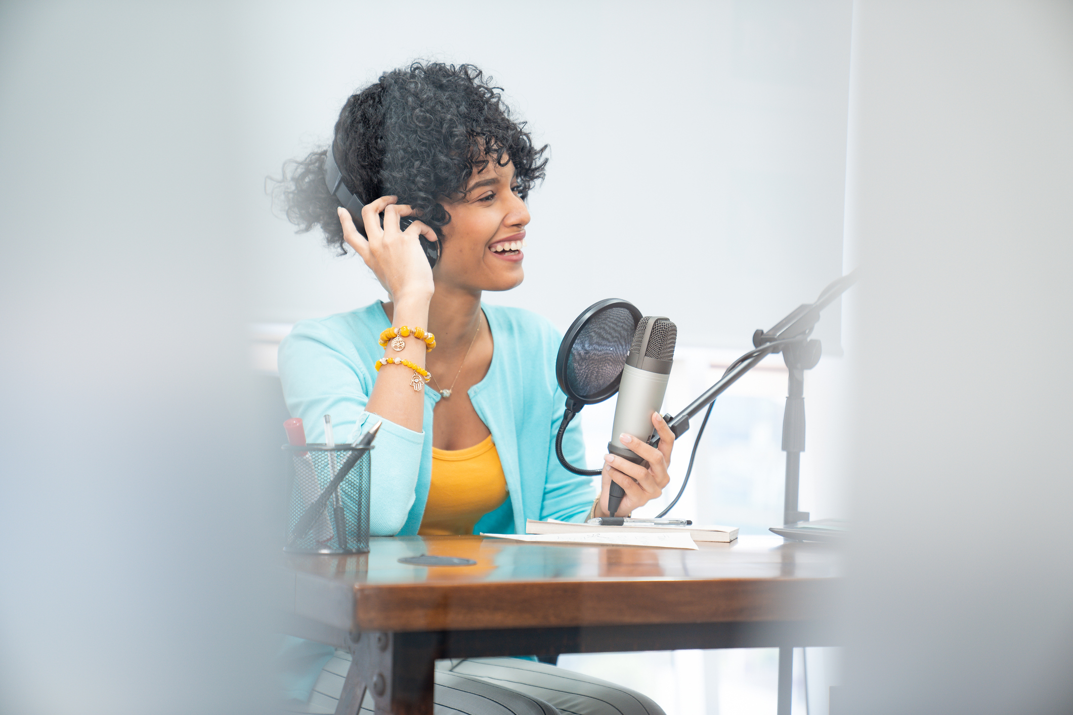 Smiling woman with headphones, grabbing an audio microphone while seated at a desk.