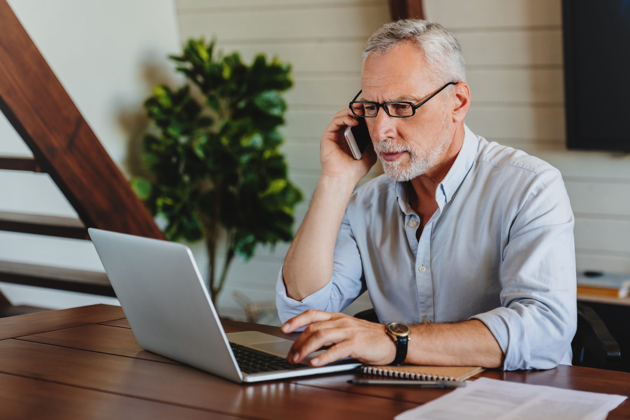 Older person at laptop talking on phone.