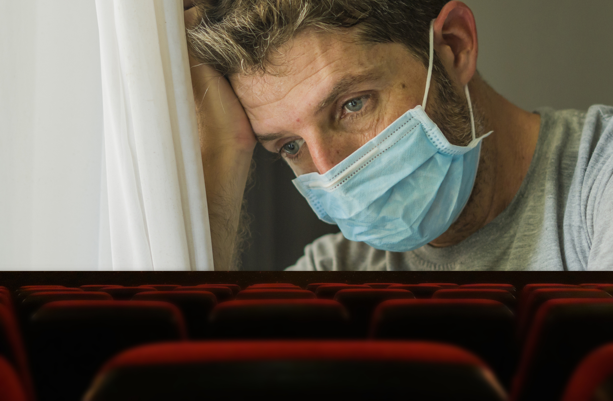 In an empty movie theater, the silver screen shows a tired person wearing a surgical face mask.