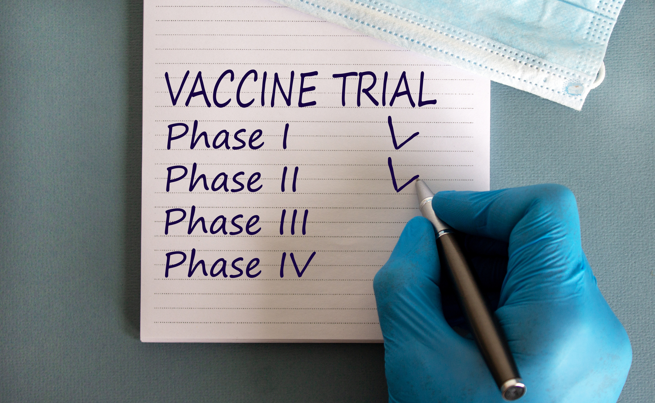 A researcher's hand checks off "phase 1 and 2" on a vaccine trial list.