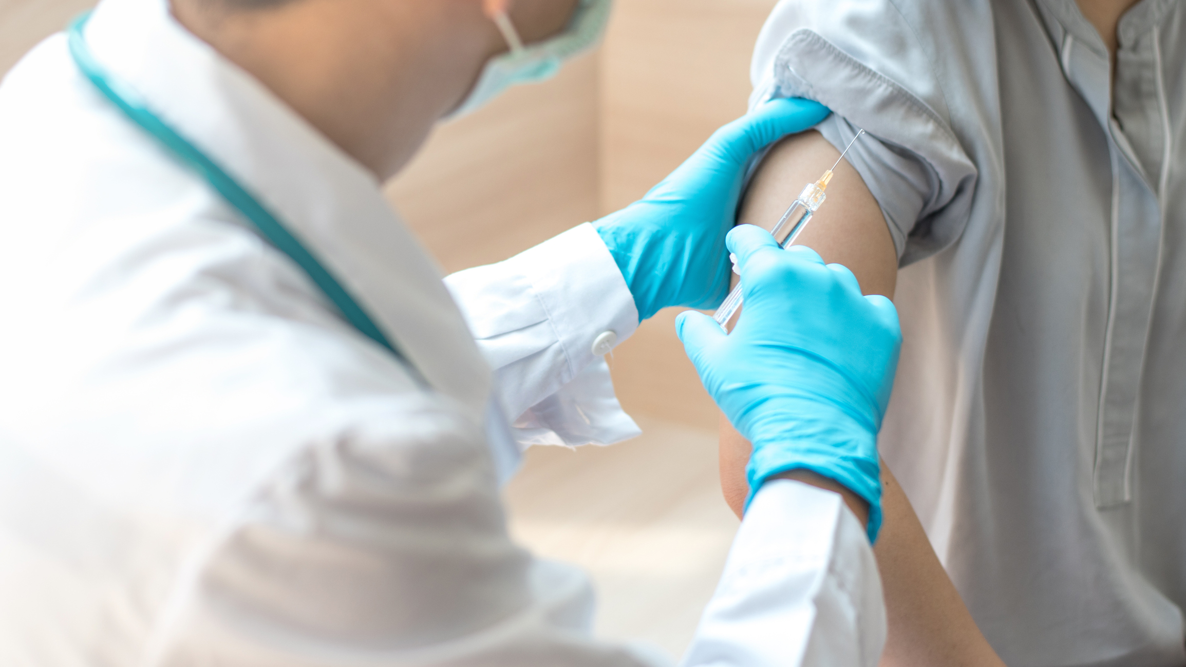 Physician holding a syringe with a needle next to a patient's arm