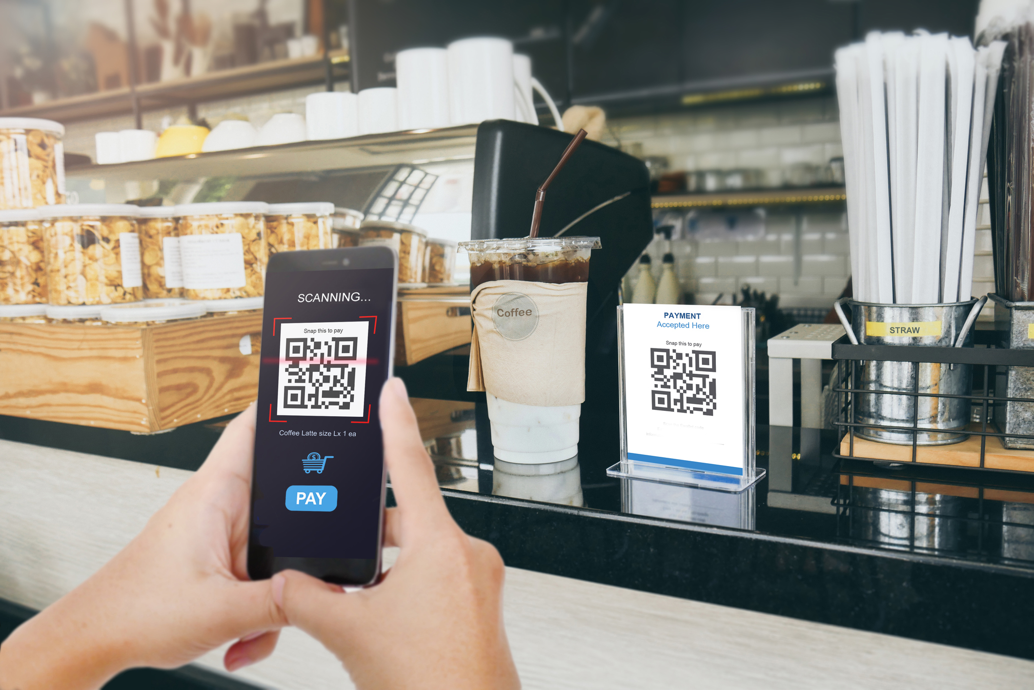 Person paying at a coffee shop using a QR code on a mobile phone.