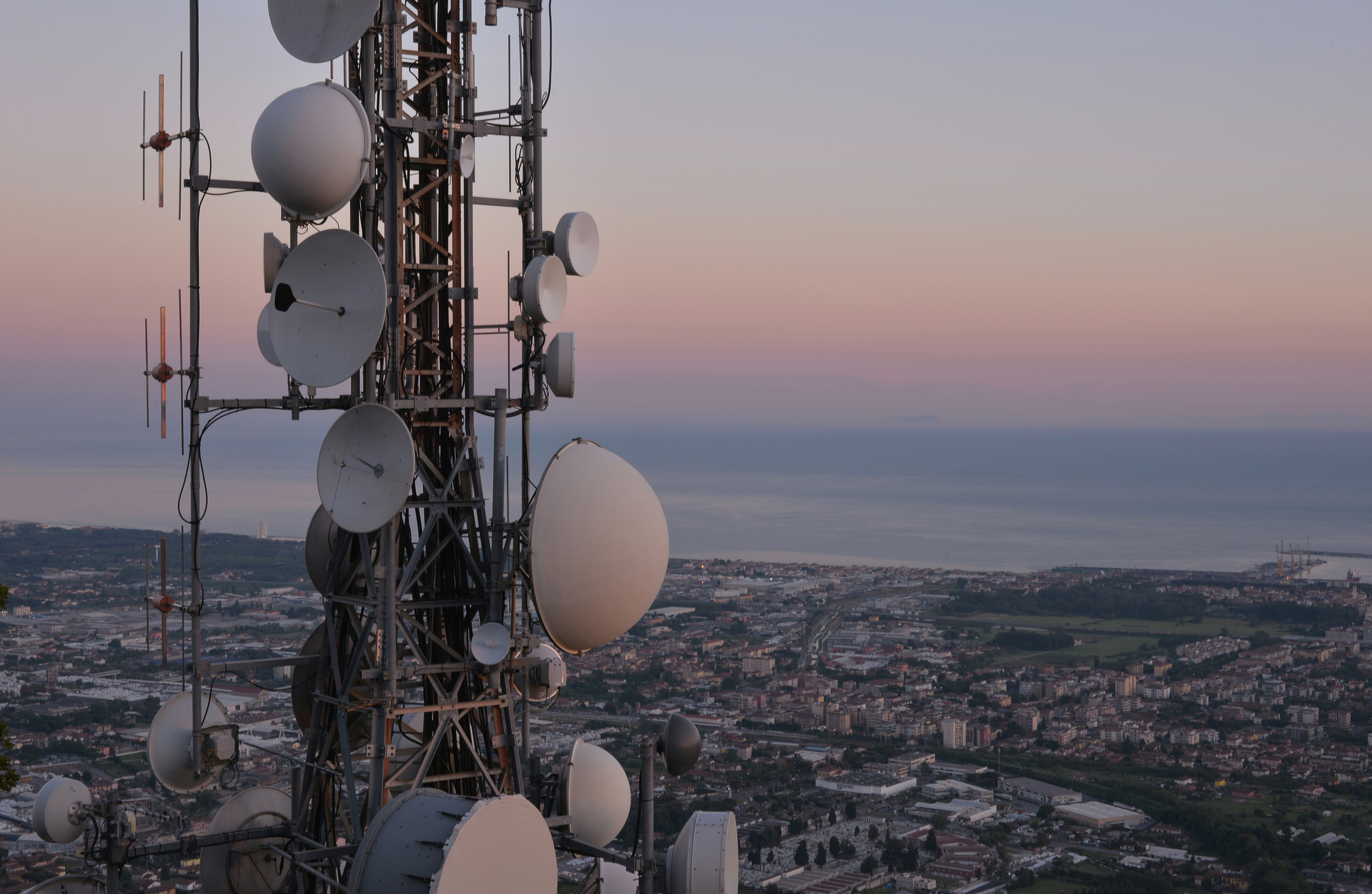 A tower laden with large radios looking over a seaside town.
