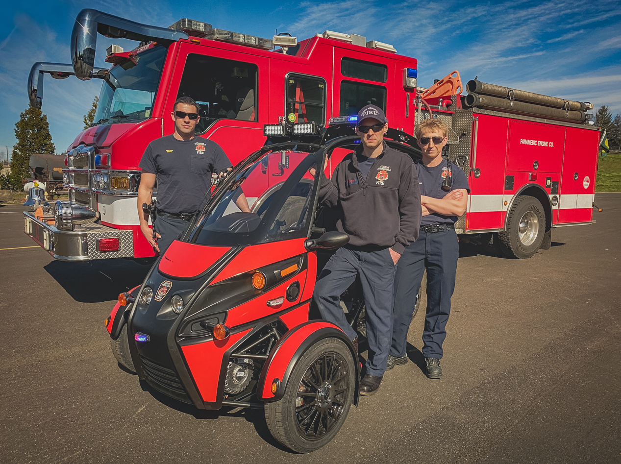 Emergency workers pose with an Arcimoto Rapid Responder in front of fire truck.