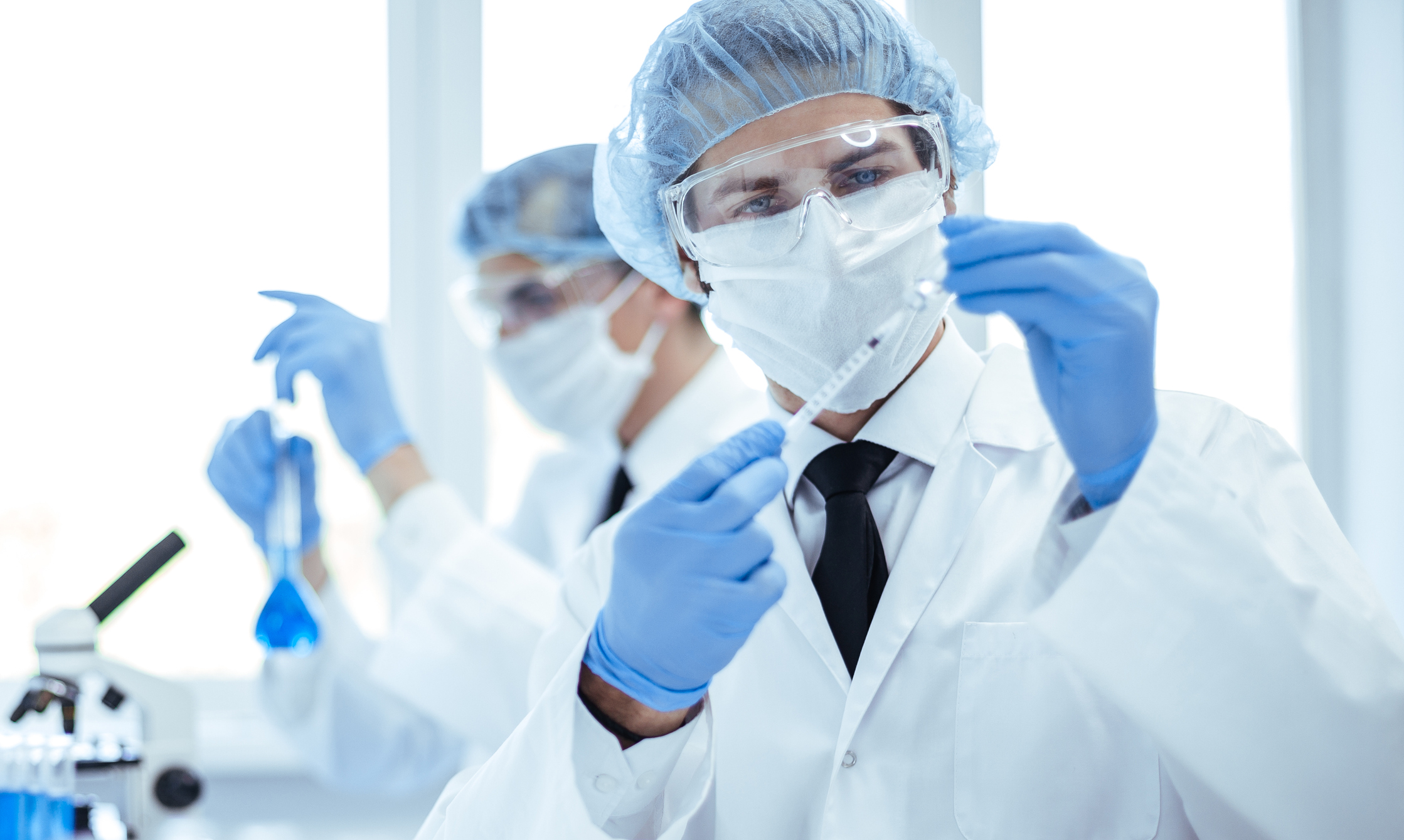 A scientist examines a syringe as another scientist examines a test tube.