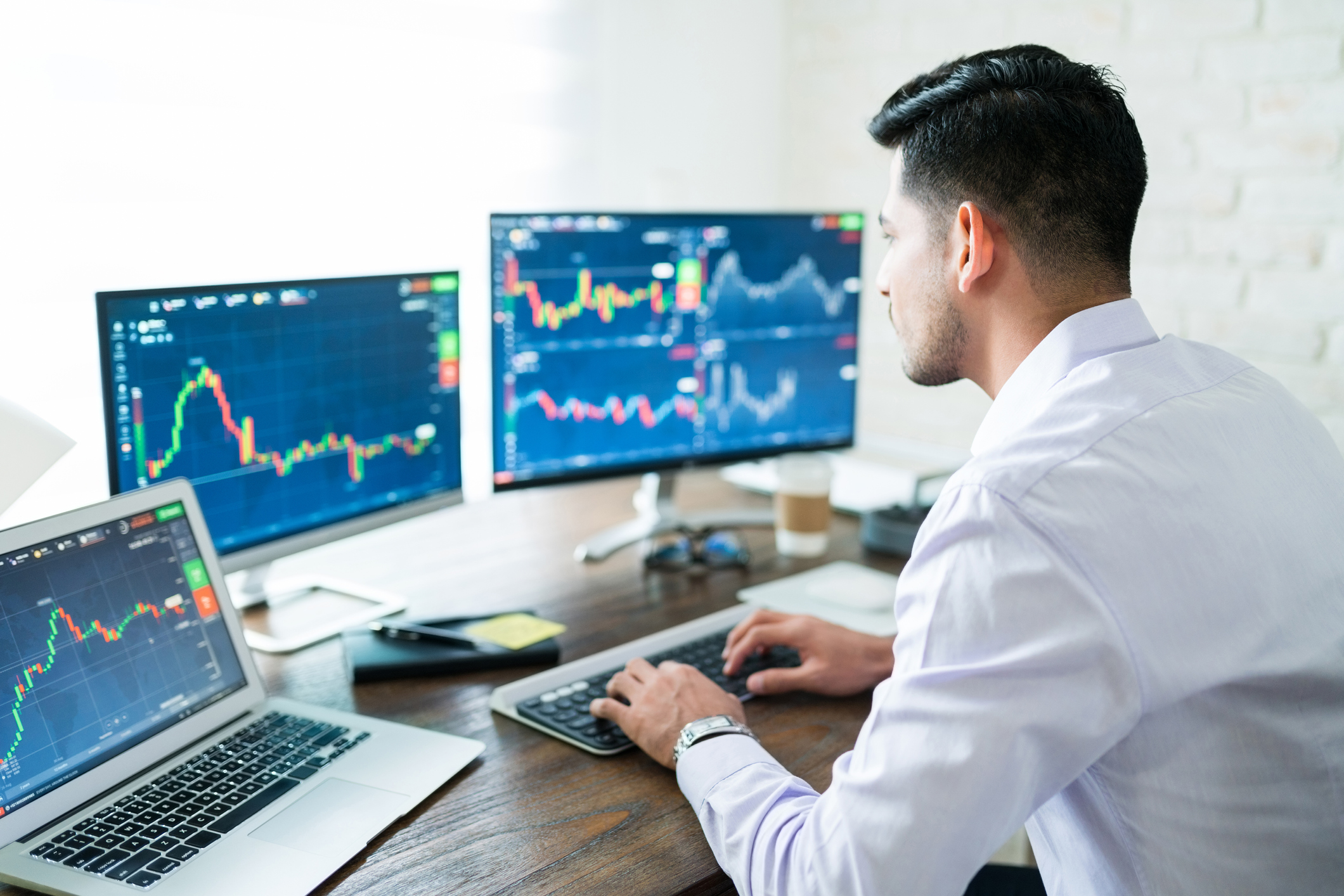 Man looking at stock charts on three computer screens