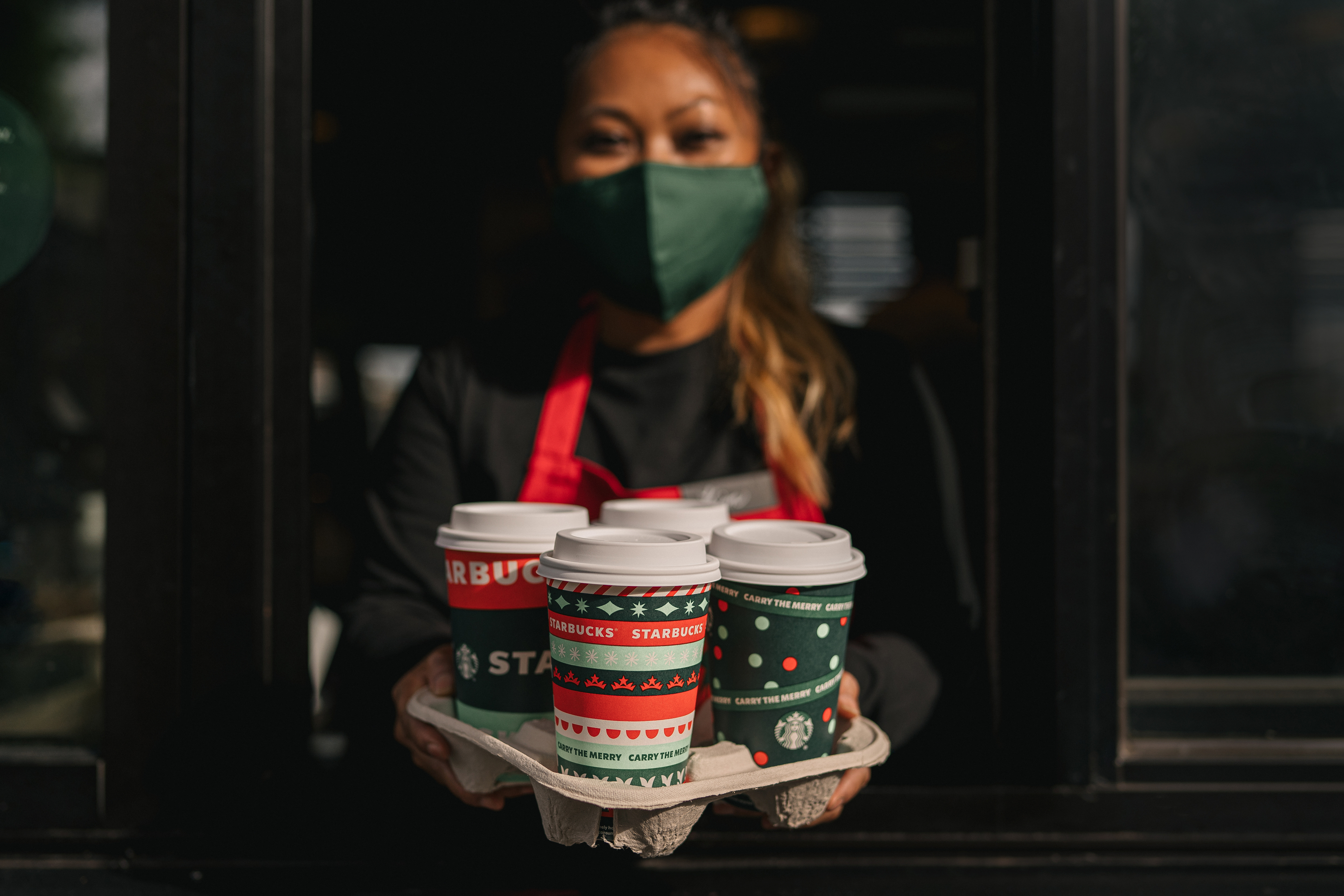 Starbucks employee displaying a tray full of drinks in festive holiday cups.