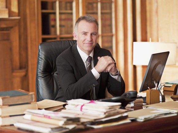 Smiling older person in suit sitting at desk. 