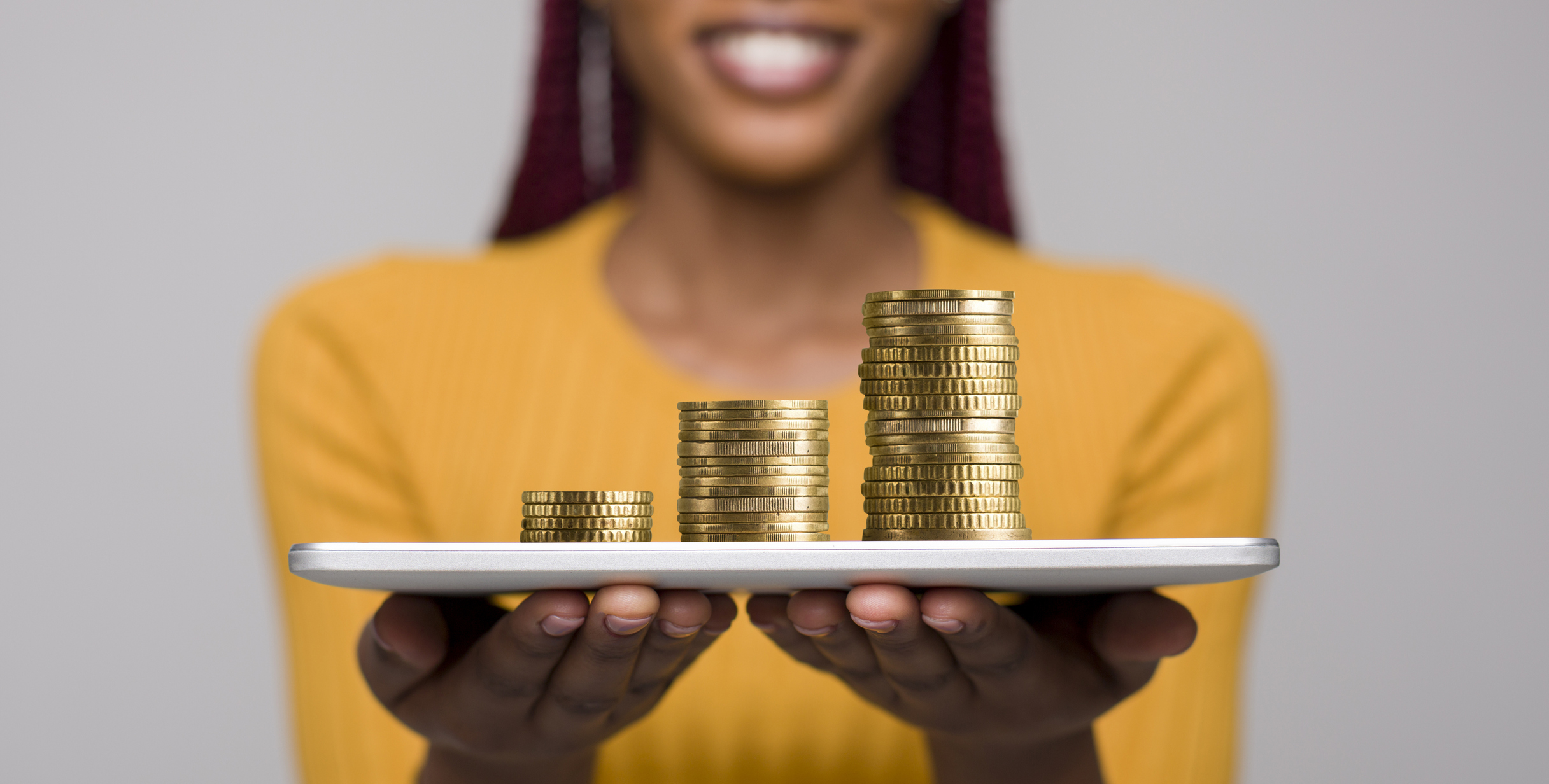 A woman holding a tablet computer with coins stacked on top of it.