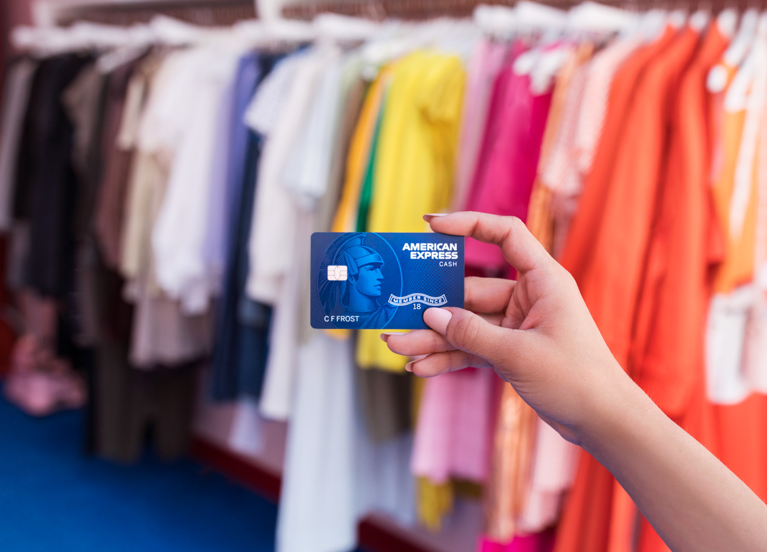 Person holding up a a blue American Express card next to a row of clothing.