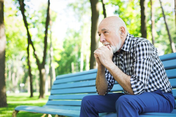 Older man sitting on park bench with thoughtful expression
