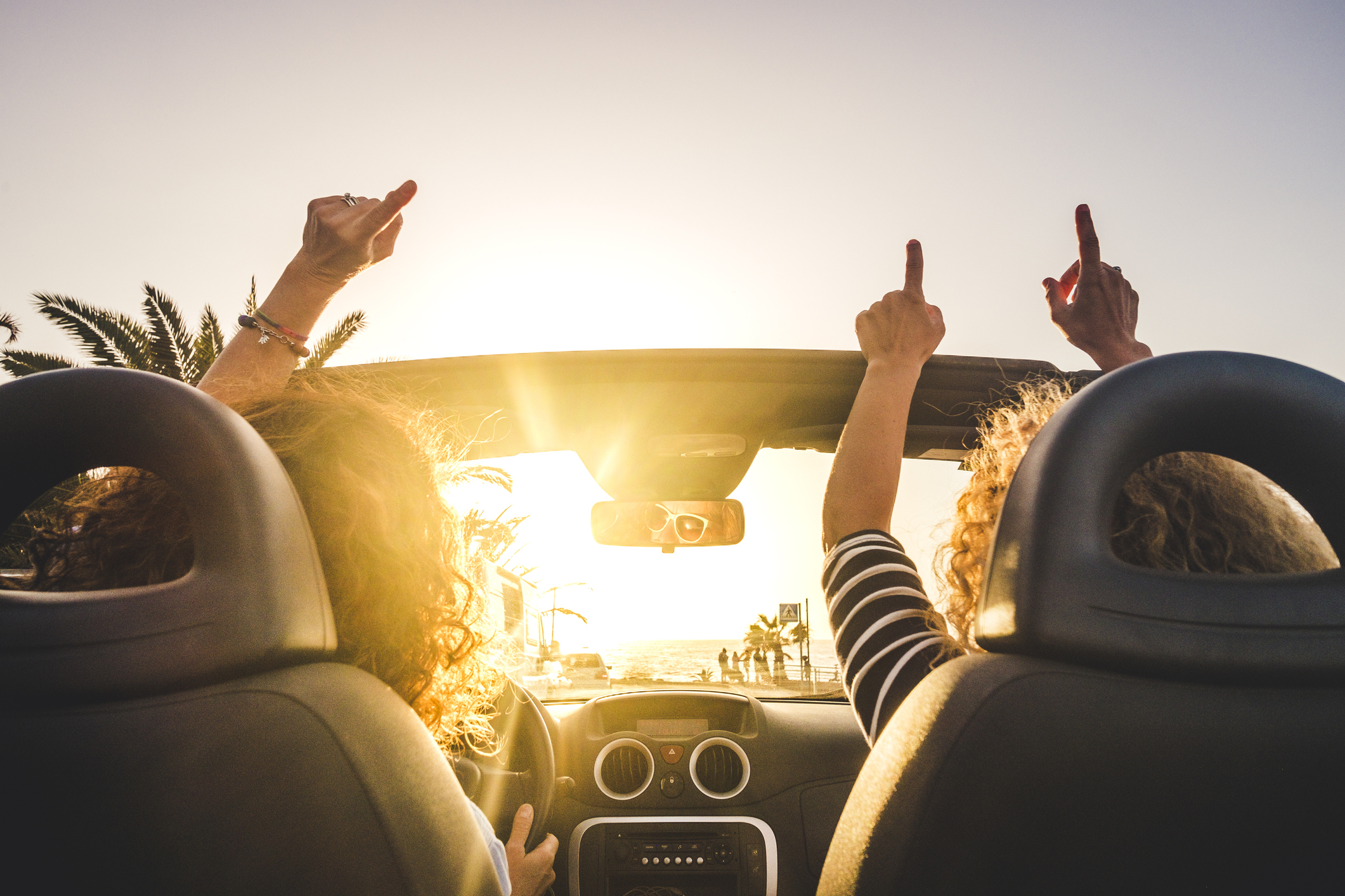Two women driving in a convertible with their hands in the air listening to music