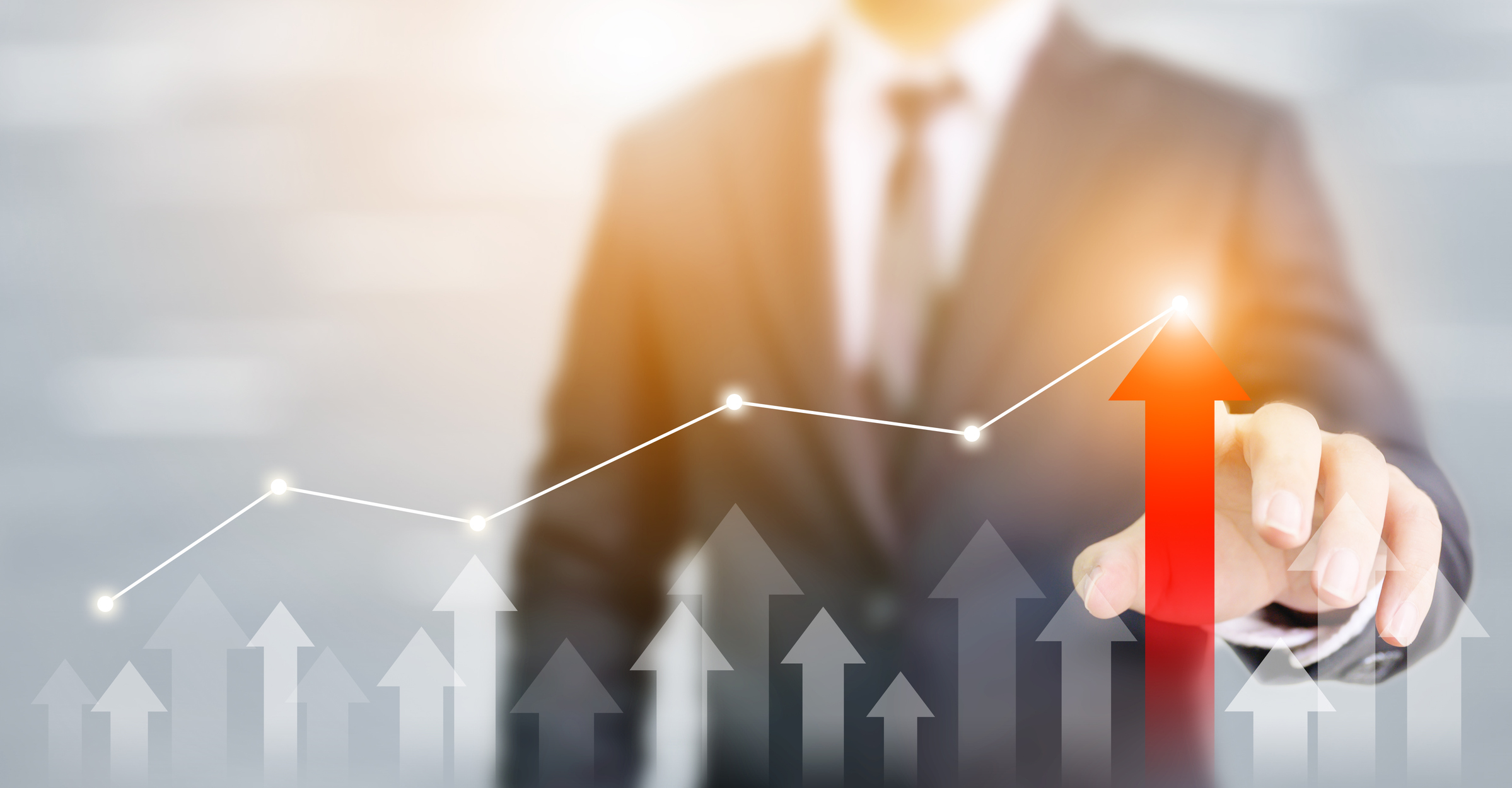 A chart line going up over arrows also pointing up as a businessman points to the tallest arrow.