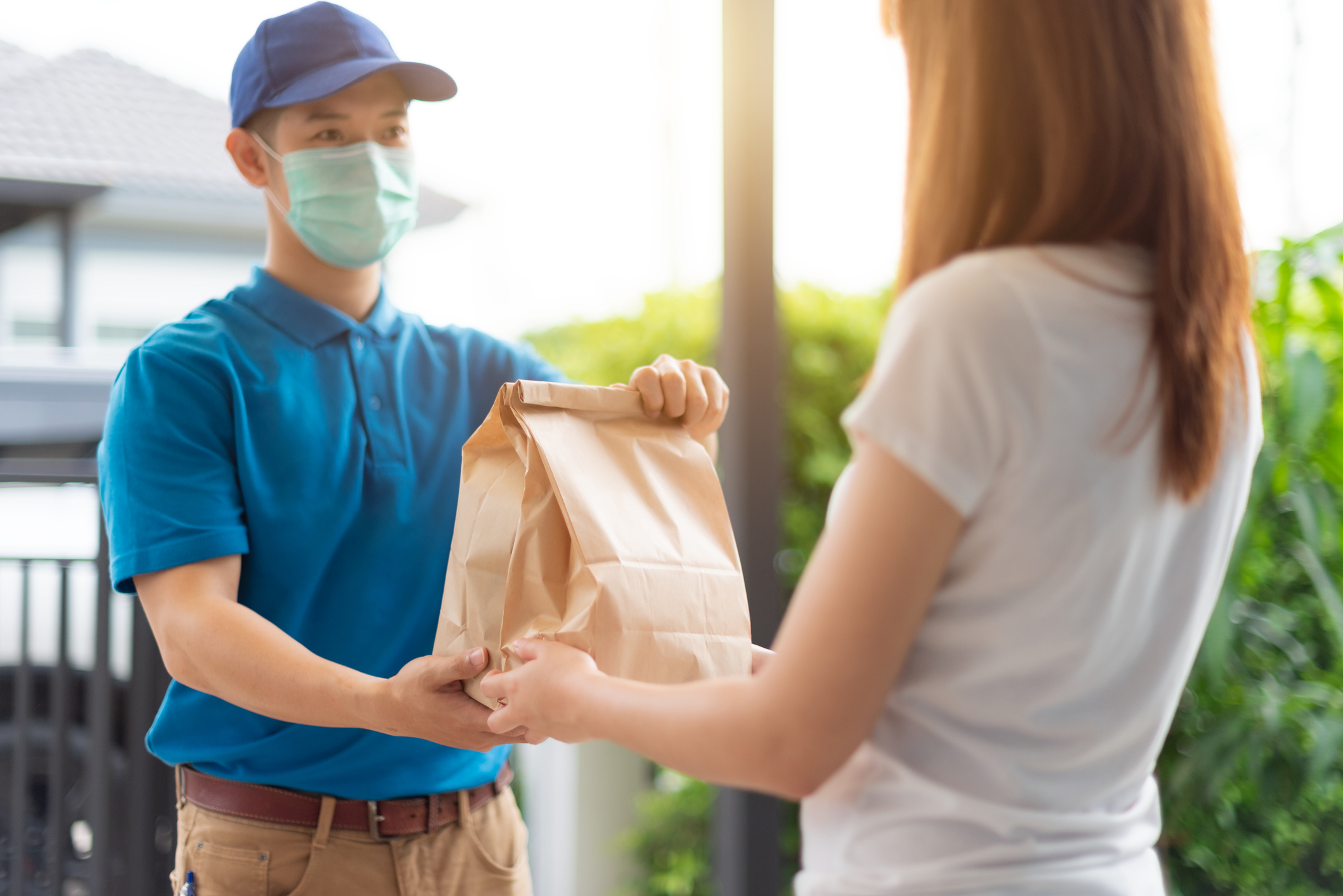 A bag of food being delivered to a customer with a mask-wearing driver.