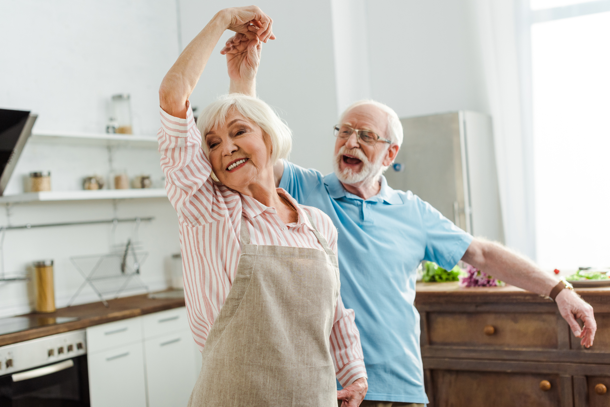 Older man and older woman in apron dancing in kitchen