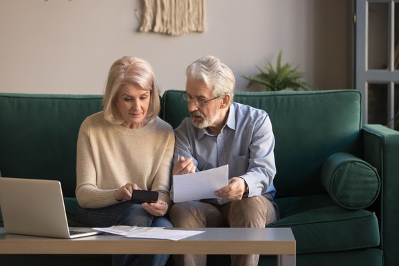 Older couple sitting on the couch look at documents and a calculator