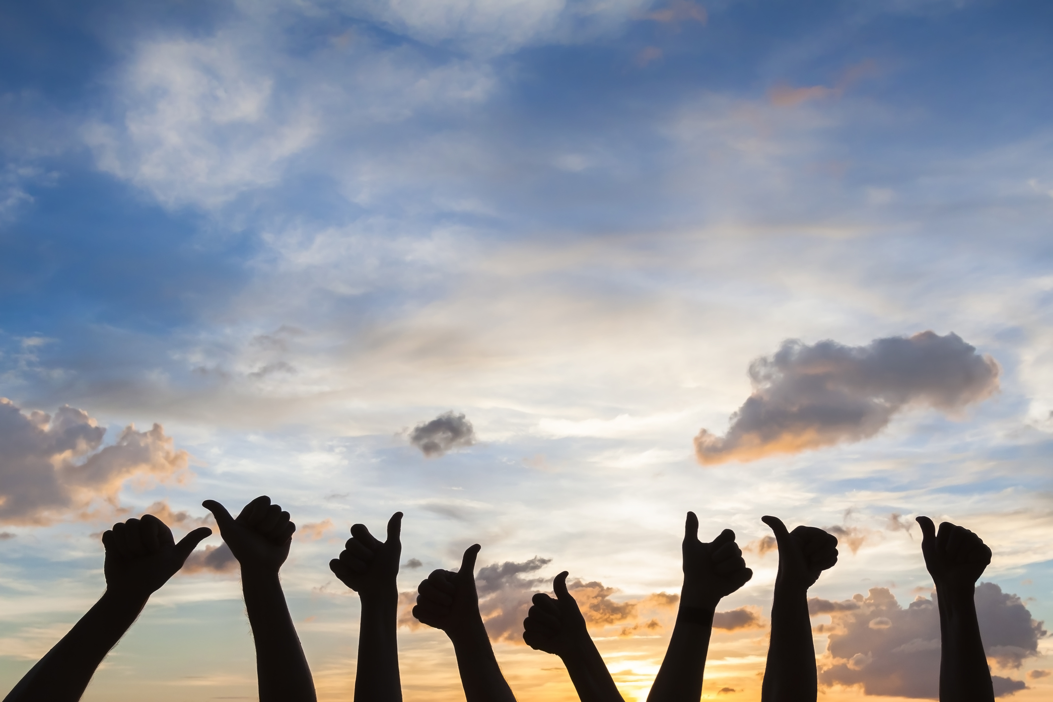 Silhouette of 8 people giving thumbs-up signals against a partly cloudy sky.