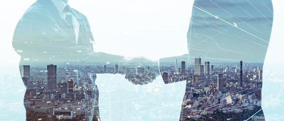 Image of two businessmen shaking hands superimposed over view of city. 