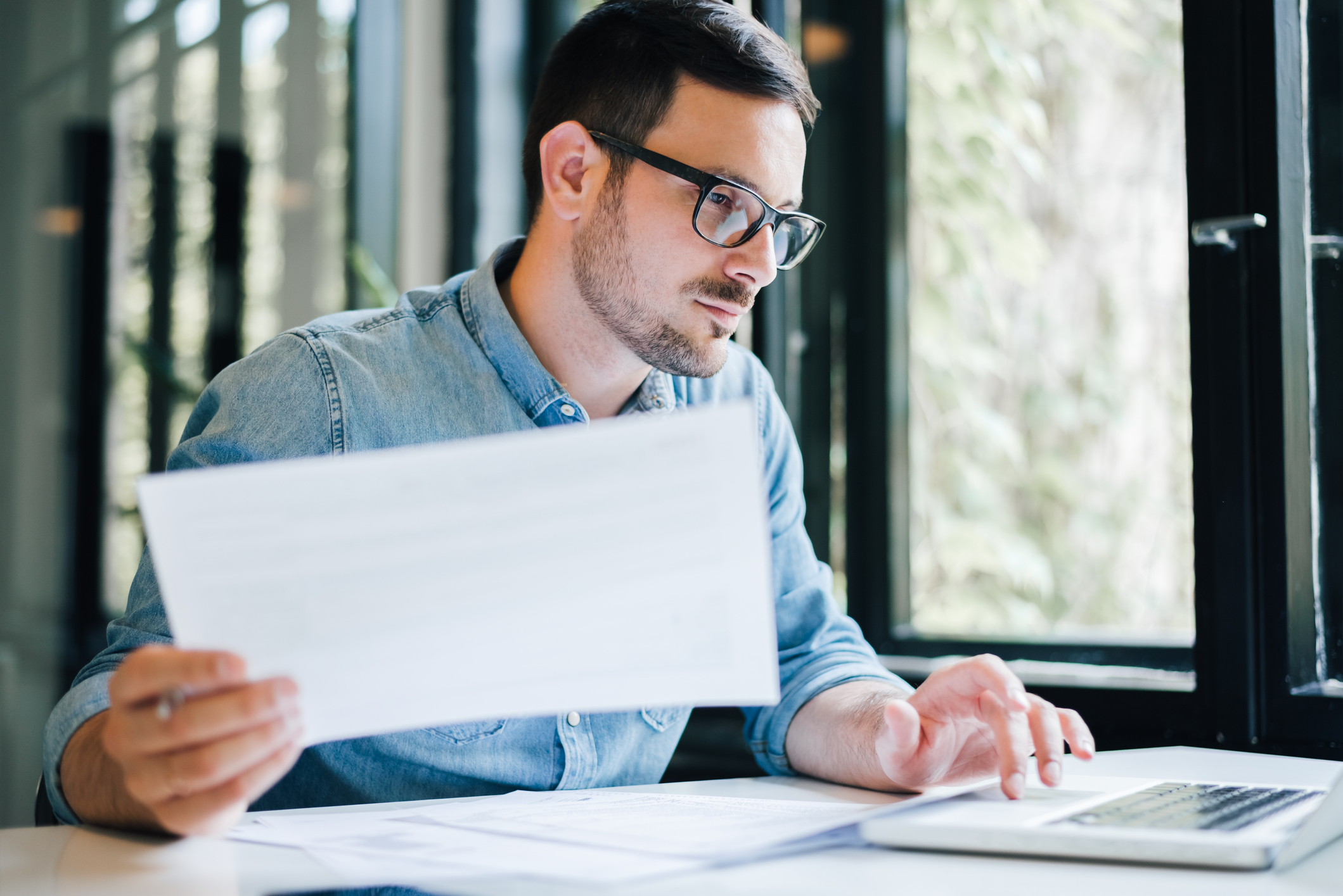 A person at a laptop holding document. 