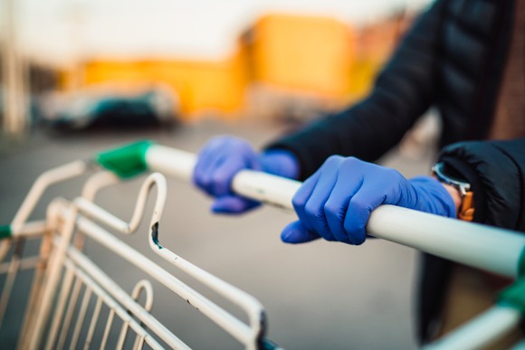 Shopping cart being pushed by gloved hands.