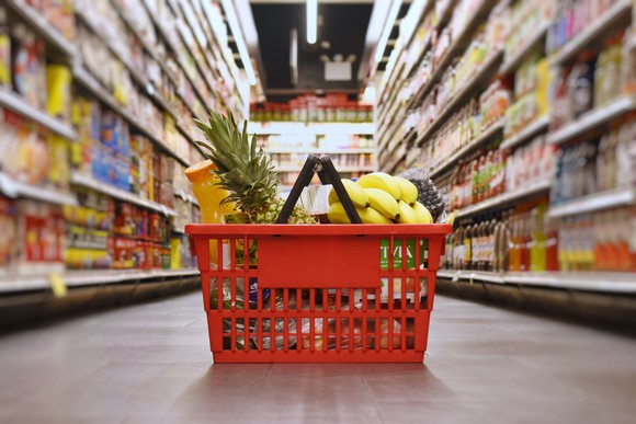 A basket filled with groceries on the floor of a grocery aisle.