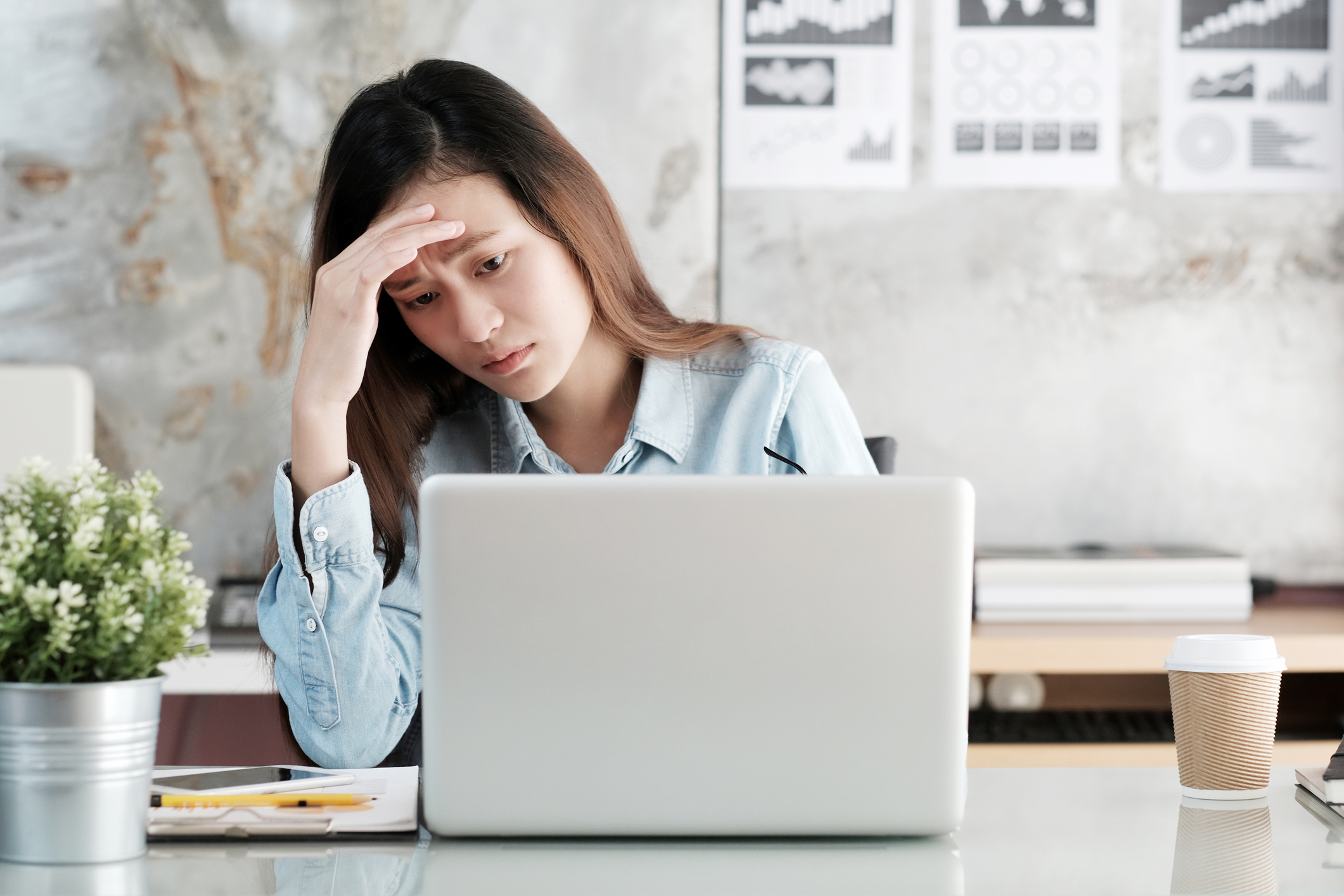 Woman at laptop resting hand on forehead and looking upset
