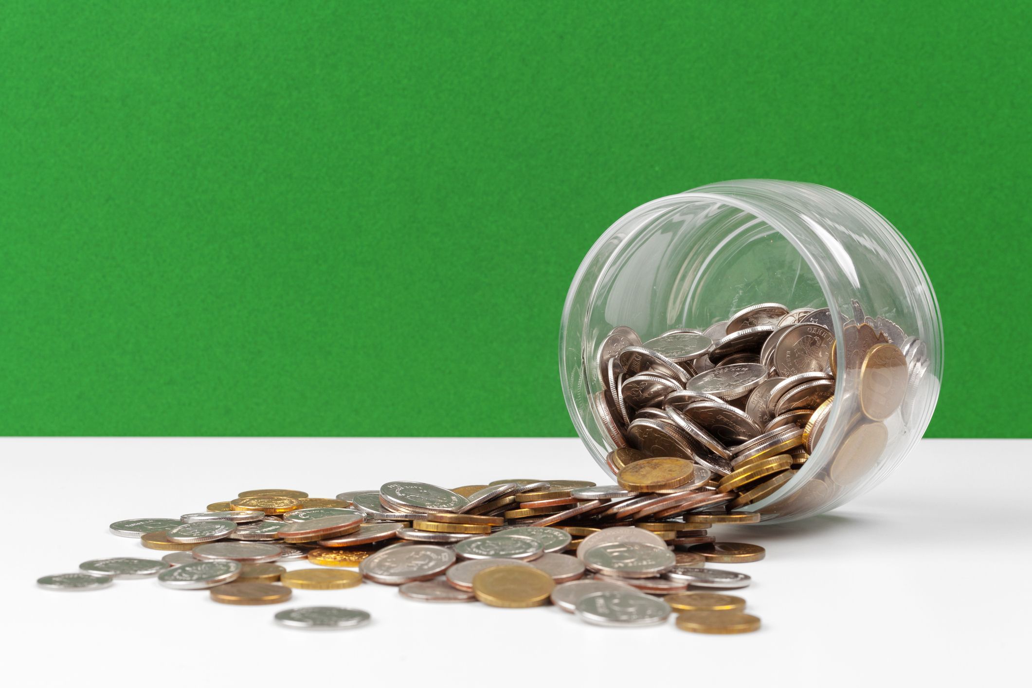 Glass jar on its side with change spilling out, against green background.