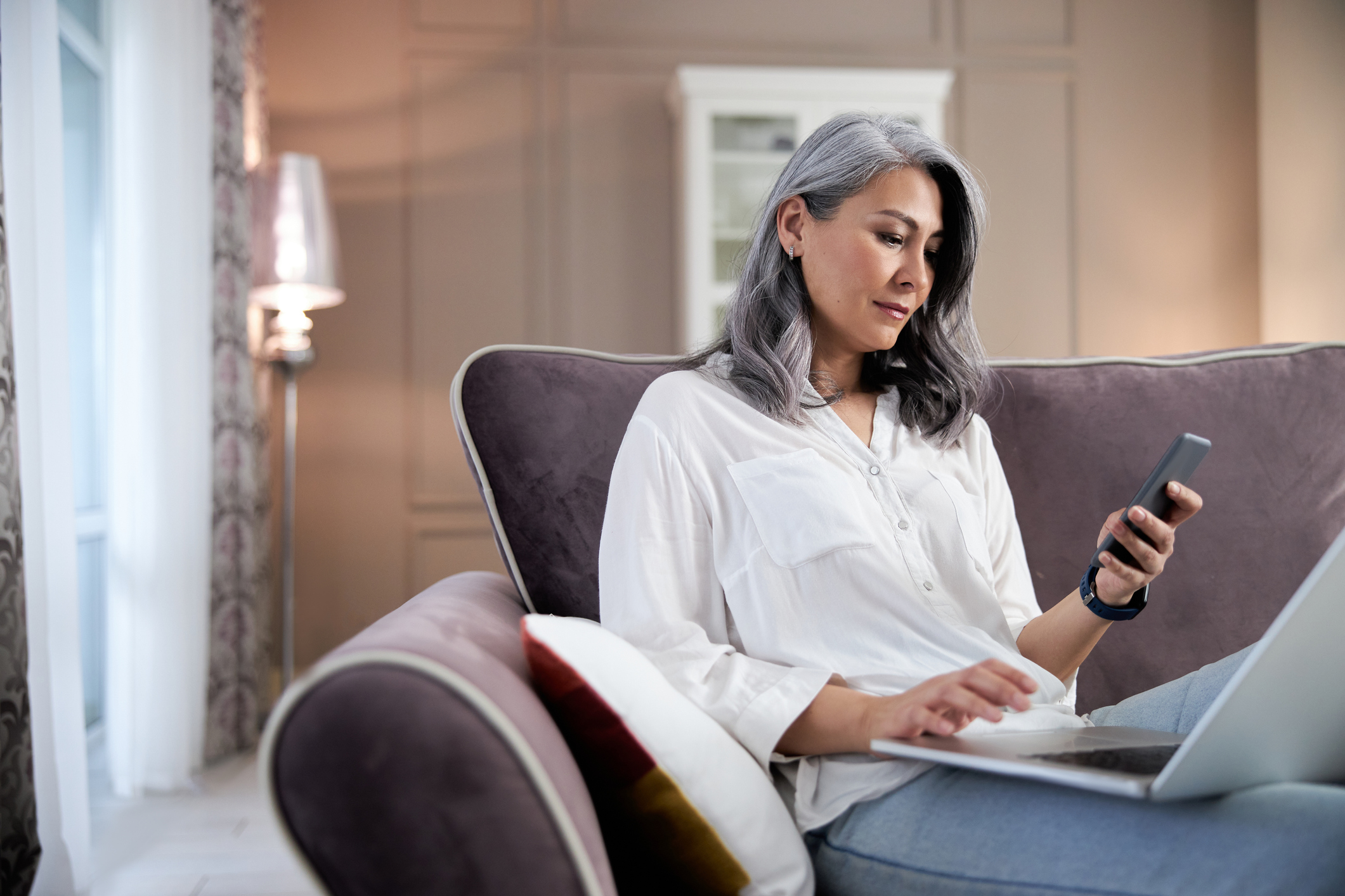 Older woman looking at her phone and laptop.