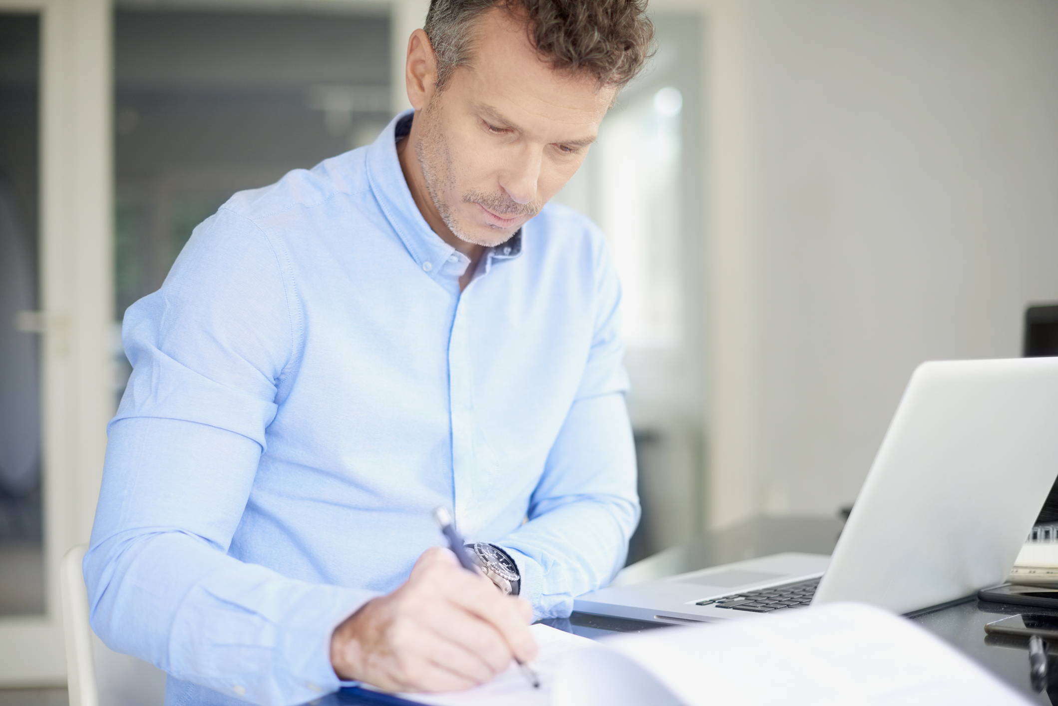 Man at laptop writing in notebook