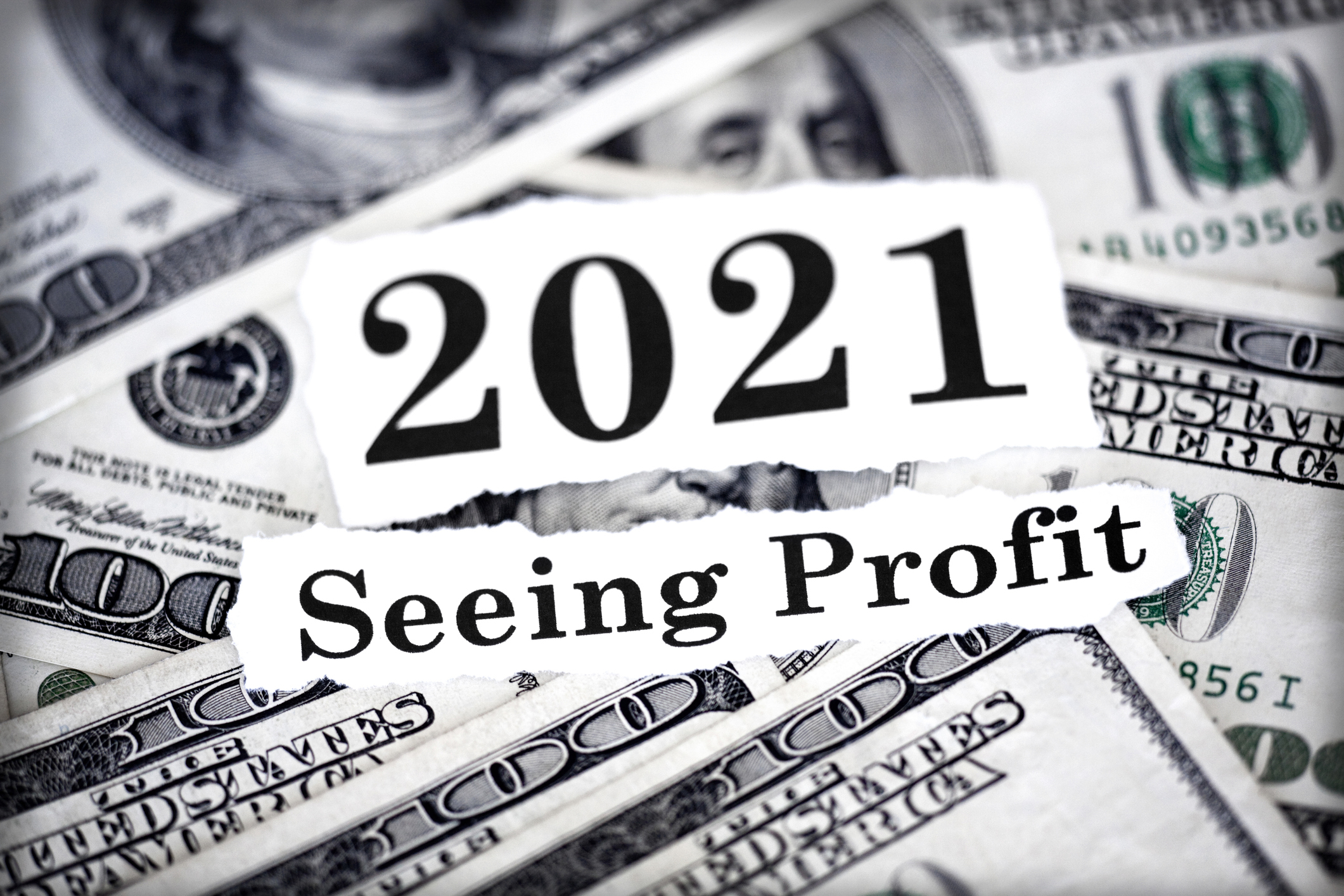 Sign that says "2021, seeing profit" amid a lot of $100 bill.