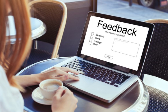 Someone sitting in front of a laptop which has a screen asking for feedback.