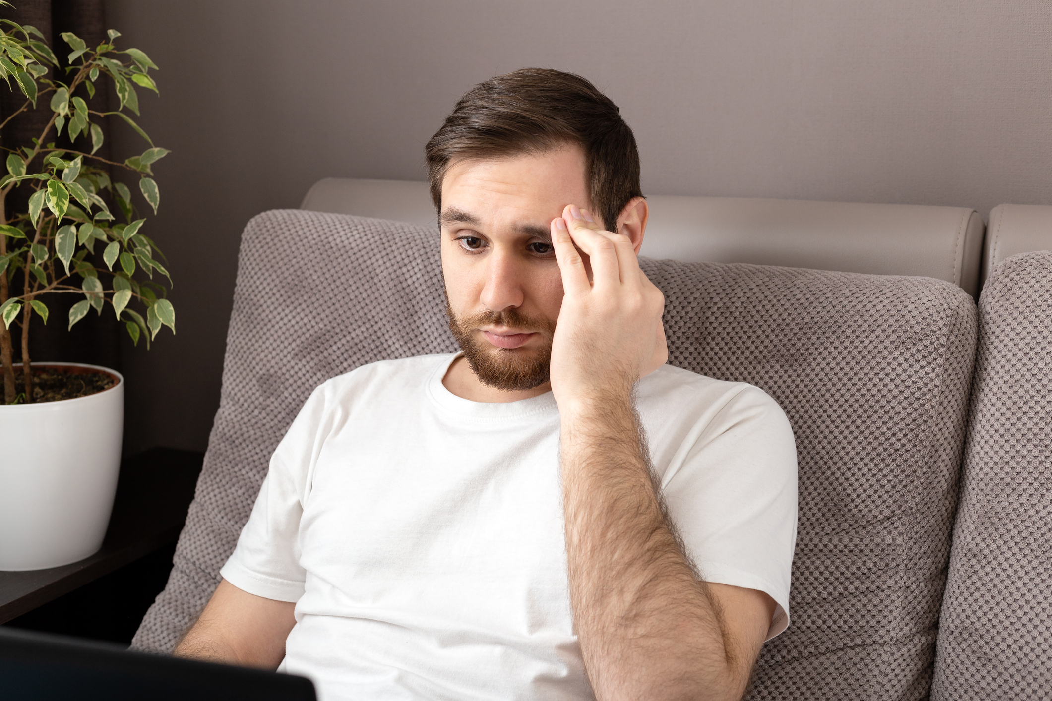A person using a laptop and holding their head while looking worried.