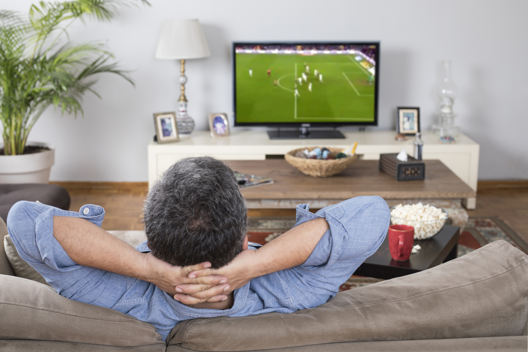 Man in a sofa watching a soccer match on TV.
