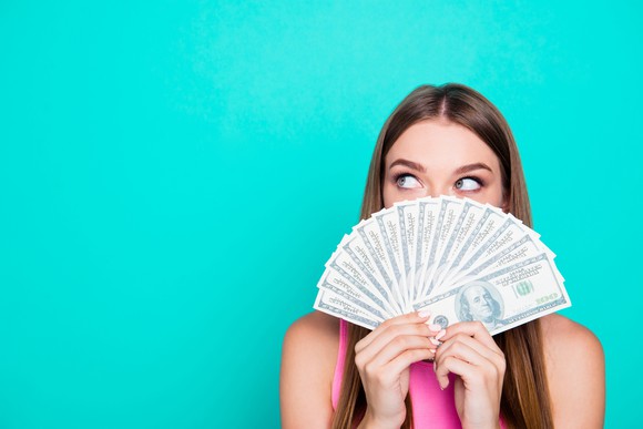 Woman holding fan of cash in front of face