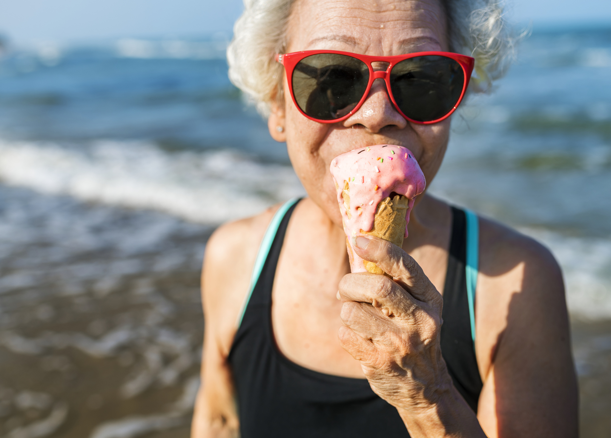 Senior woman in red sunglasses eating a strawberry ice cream cone.