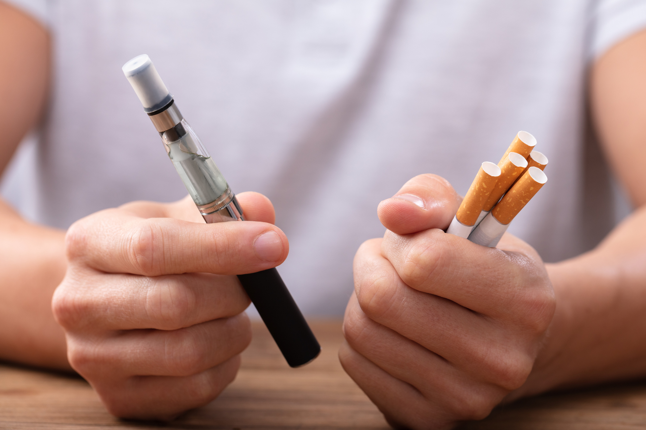 A man holds an e-cigarette and a bundle of cigarettes.