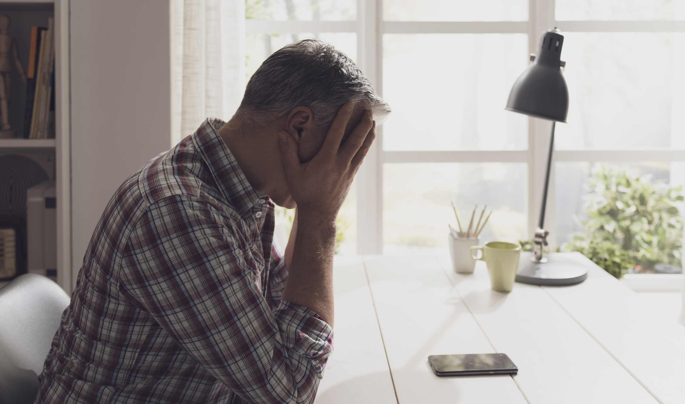 Older man sitting at table, covering his face