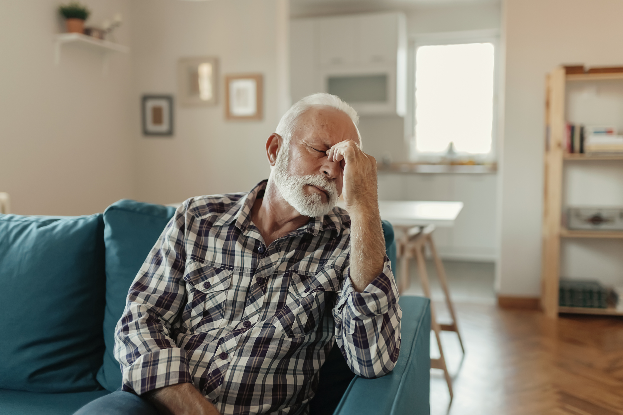Older man seated on coach closing eyes and pinching nose