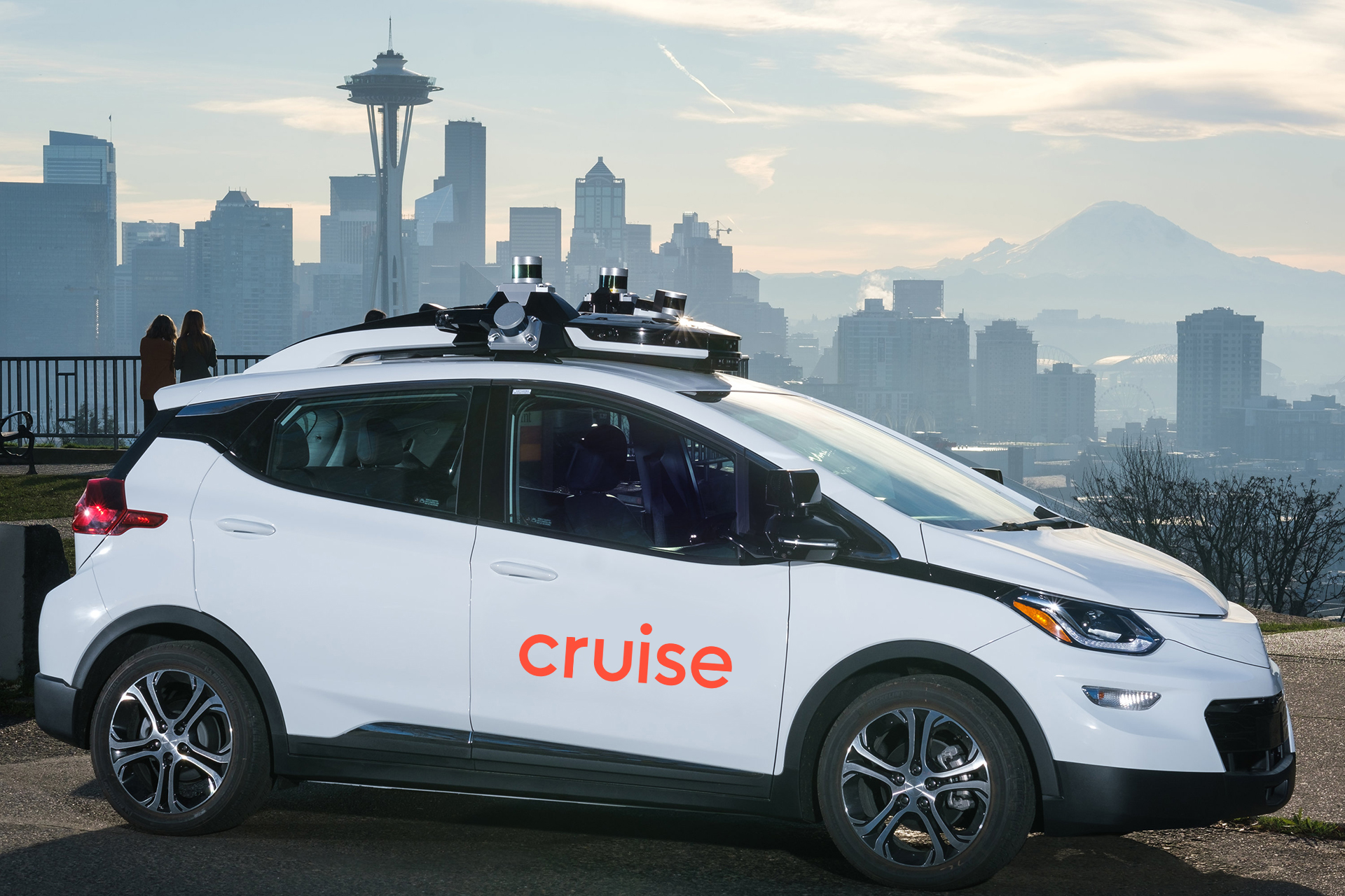 A white Chevrolet Bolt EV with Cruise logos and visible self-driving sensor hardware.