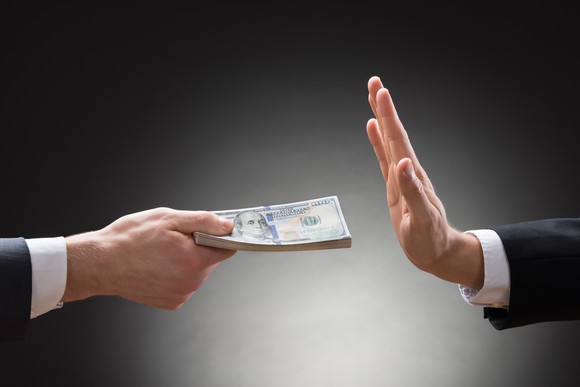 A businessman refusing a stack of cash offered by another businessman.