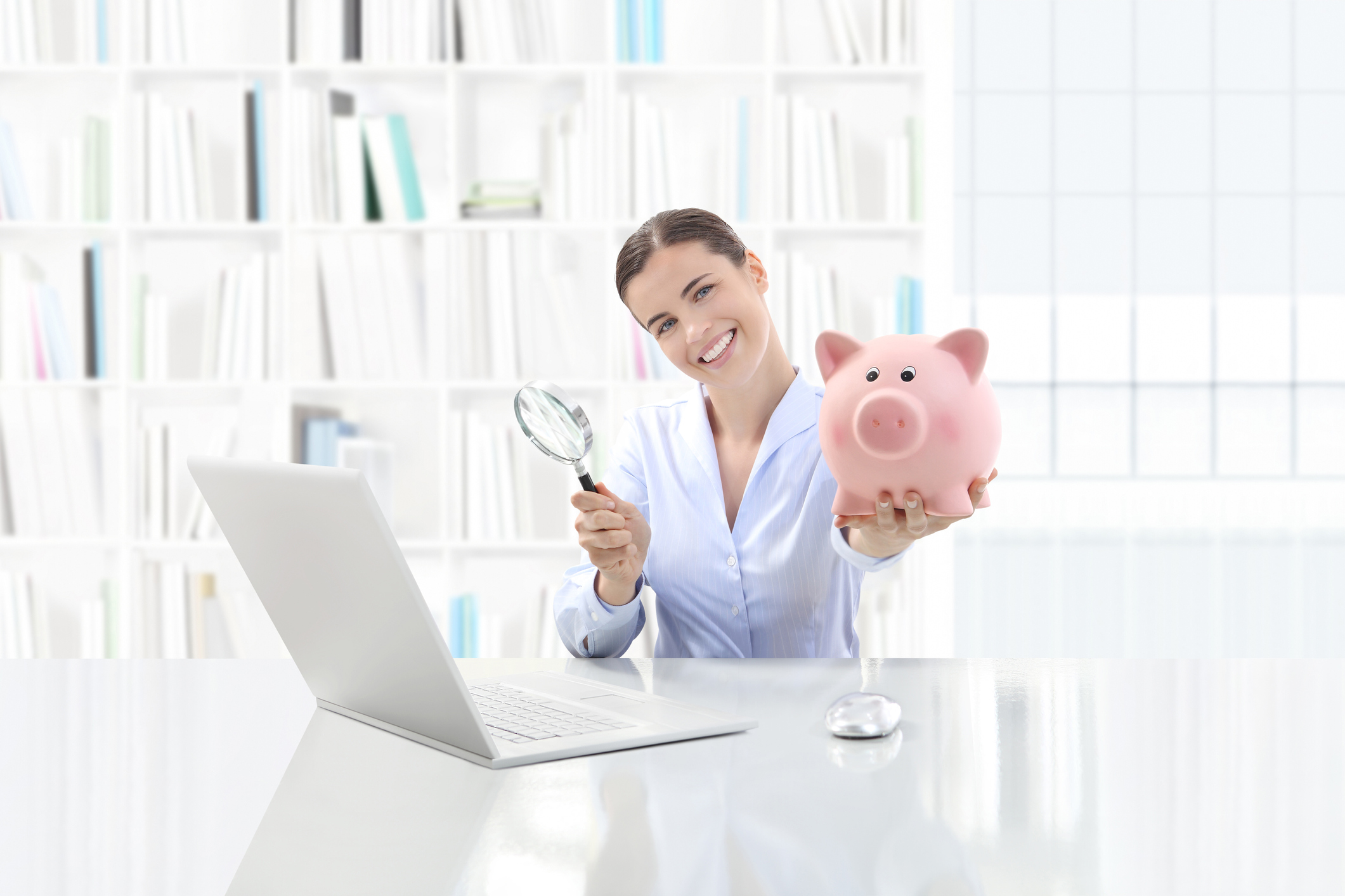 A woman with a piggy bank and a magnifying glass in front of her laptop.