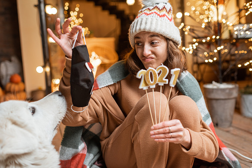 A woman with her dog holding up 2021 candles and a face covering. 