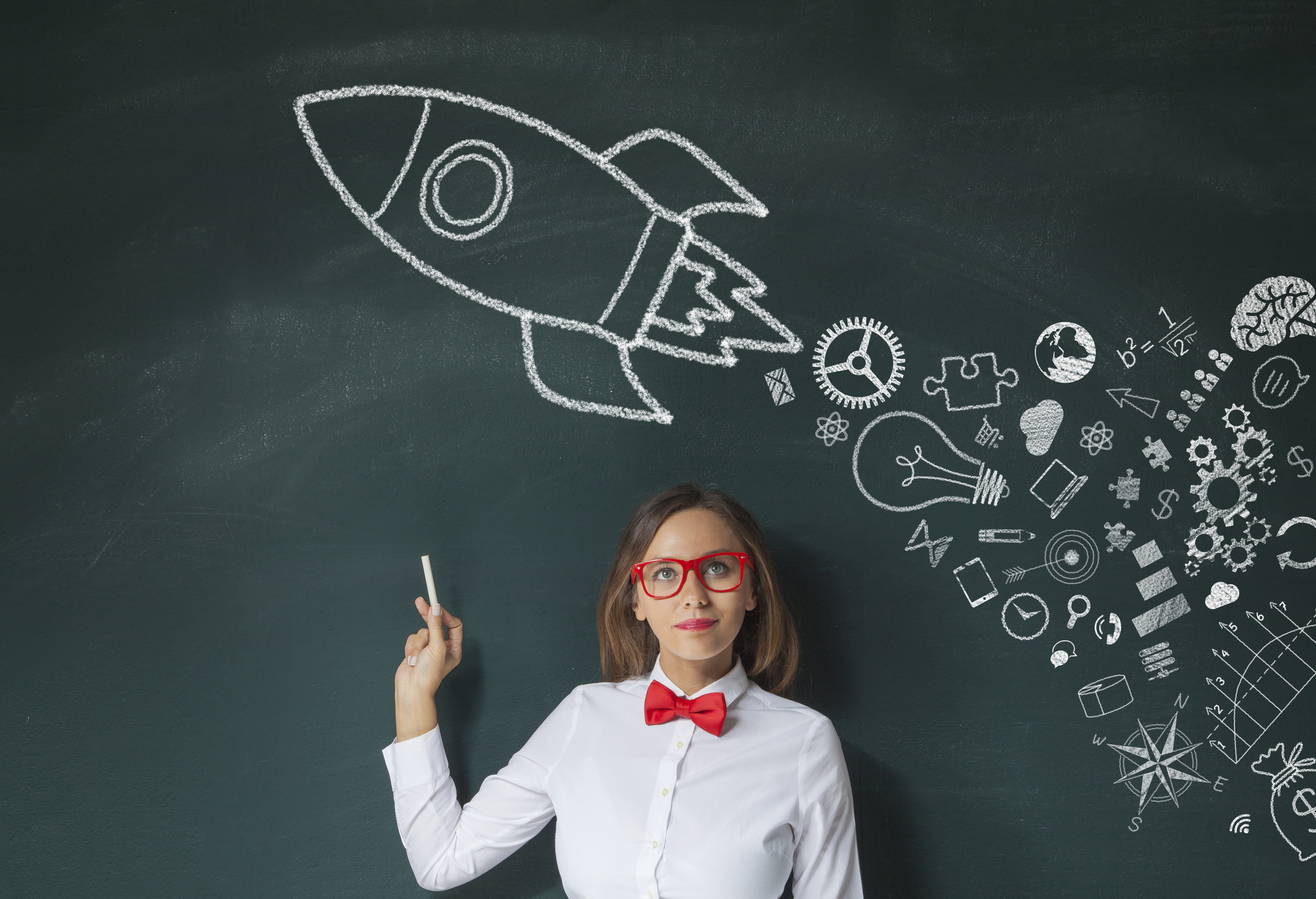 A young woman wearing a red bowtie and white shirt draws an innovation-powered rocket on a large chalkboard.